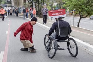 duas pessoas andando com equipamentos adaptados: triciclo e skate