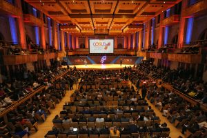 fotografia colorida de Sala São Paulo - pessoas sentadas em auditório, no palco um grande painel com o nome do evento "COSUD".