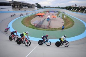foto colorida de velódrome com quatro atletas em suas bicicletas durante disputa